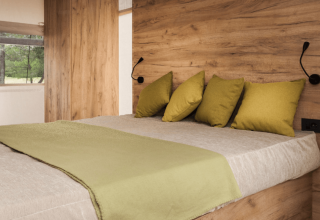 Lit confortable avec coussins verts et mur en bois au Lodge de Montagne Petite, Gulperberg, Pays-Bas.