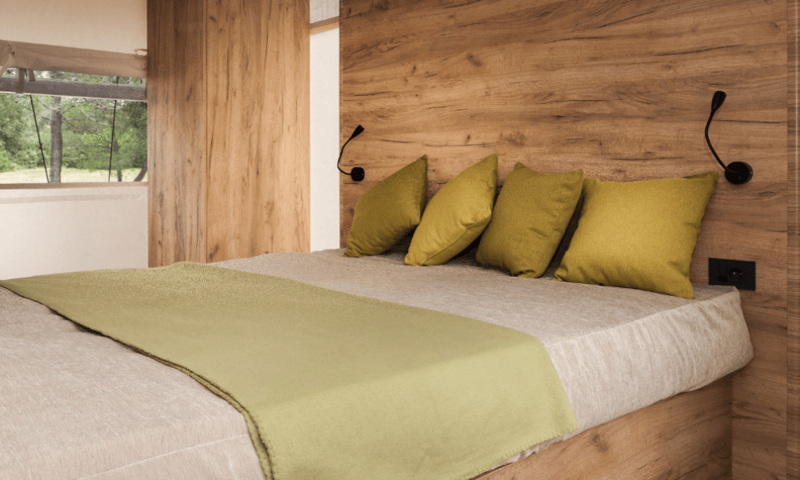 Cama acogedora con cojines verdes y pared de madera en Lodge de Montagne Petite, Gulperberg, Países Bajos.