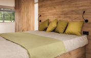 Cama acogedora con cojines verdes y pared de madera en Lodge de Montagne Petite, Gulperberg, Países Bajos.