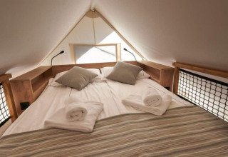 Smukt indrettet seng i Lodge de Montagne Petite safaritelten på Gulperberg, Holland, med rene håndklæder.