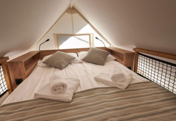 Letto accogliente nella tenda safari Lodge de Montagne Petite a Gulperberg, Paesi Bassi, con asciugamani arrotolati.