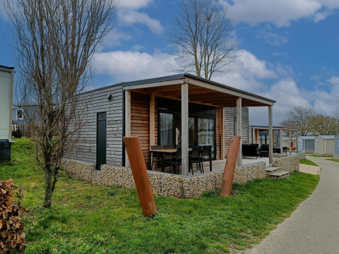 Foto der Grandeur Chalet-Lodge mit moderner Holzfassade, überdachter Veranda und Gartenstühlen im Grünen.