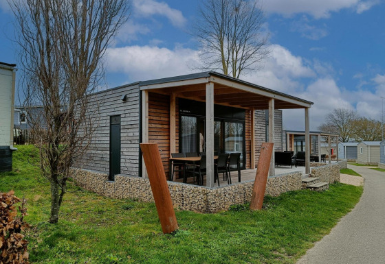 Foto der Grandeur Chalet-Lodge mit moderner Holzfassade, überdachter Veranda und Gartenstühlen im Grünen.