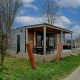 Billede af Grandeur Chalet-lodgen med træfacade, overdækket terrasse og udendørs siddeplads på en grøn græsplæne.