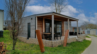 Afbeelding van de Grandeur Chalet-lodge met houten gevel, overdekte veranda en zitgedeelte buiten op het gras.