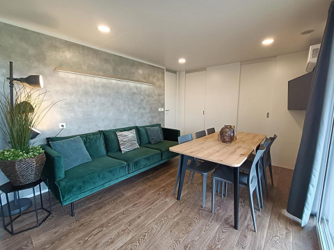 Wohnzimmer im Grandeur Chalet am Gulperberg, Niederlande, mit grüner Couch, Esstisch und moderner Deko.