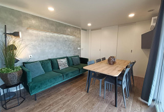 Wohnzimmer im Grandeur Chalet am Gulperberg, Niederlande, mit grüner Couch, Esstisch und moderner Deko.
