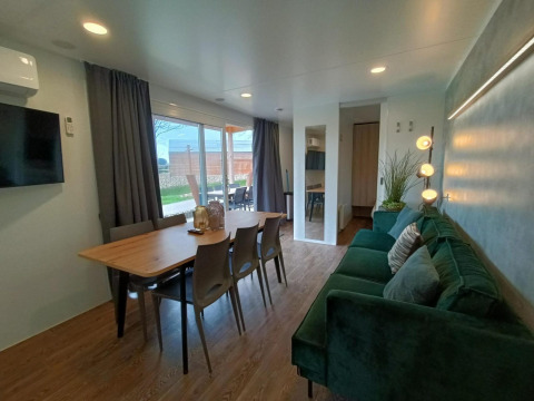 Sala y comedor modernos en Grandeur Chalet de Gulperberg, Países Bajos, con sofá verde y gran ventana.