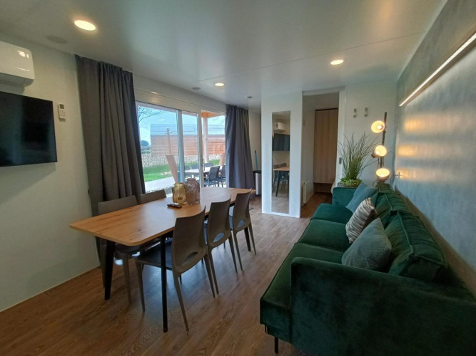 Moderne woon- en eetruimte in Grandeur Chalet op Gulperberg, Nederland, met groene bank en grote ramen.