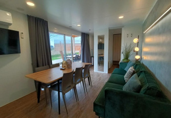 Moderne leef- en eetruimte in Grandeur Chalet op Gulperberg, Nederland, met groene zetel en veel licht.