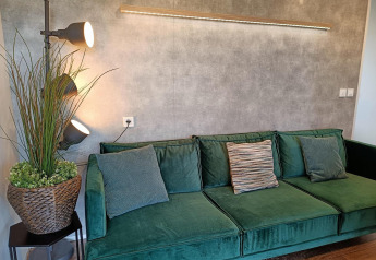 Groene zetel met kussens, staande lamp en plant in Grandeur Chalet te Gulperberg, Nederland.