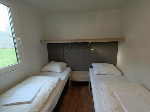 Dos camas individuales en una habitación con suelo de madera y ventana en Grandeur Chalet, Gulperberg, Países Bajos.
