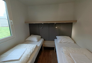 Zwei Einzelbetten in einem Zimmer mit Holzfußboden und Fenster im Grandeur Chalet, Gulperberg, Niederlande.