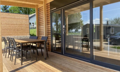 Geräumige Terrasse des Grandeur Chalets am Gulperberg in den Niederlanden mit Holzmöbeln und Glasfront.