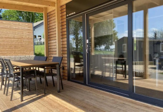 Geräumige Terrasse des Grandeur Chalets am Gulperberg in den Niederlanden mit Holzmöbeln und Glasfront.