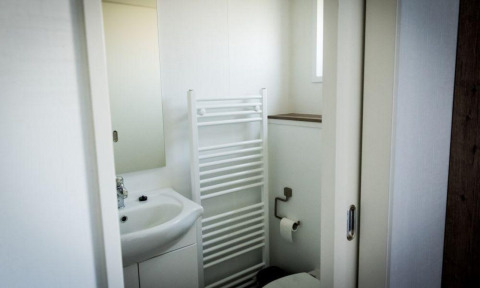 Baño de lodge con lavabo y espejo, radiador toallero y un inodoro con portarrollos en la pared.