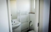 Baño de lodge con lavabo y espejo, radiador toallero y un inodoro con portarrollos en la pared.