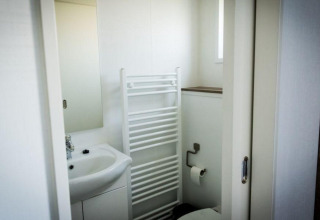 Salle de bain d'un lodge avec lavabo, miroir et radiateur sèche-serviettes devant les toilettes.
