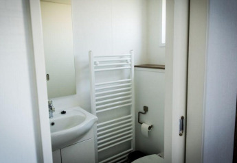 Salle de bain d'un lodge avec lavabo, miroir et radiateur sèche-serviettes devant les toilettes.