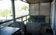 Terraza cubierta de lodge con muebles de mimbre, mesa de comedor y vistas a árboles y casas móviles.