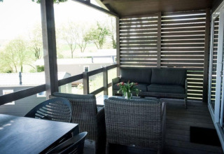 Terrazza coperta di un lodge con mobili in vimini, tavolo da pranzo e vista su alberi e case mobili.
