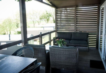 Overdekt terras bij een lodge met rotan zitmeubels, eettafel en zicht op bomen en chalets rondom.