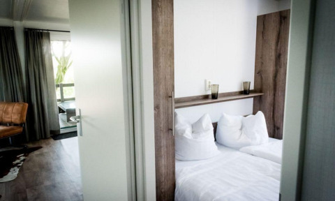 Habitación moderna de lodge con cama doble, ropa de cama blanca, cortinas gruesas y un sillón de cuero.