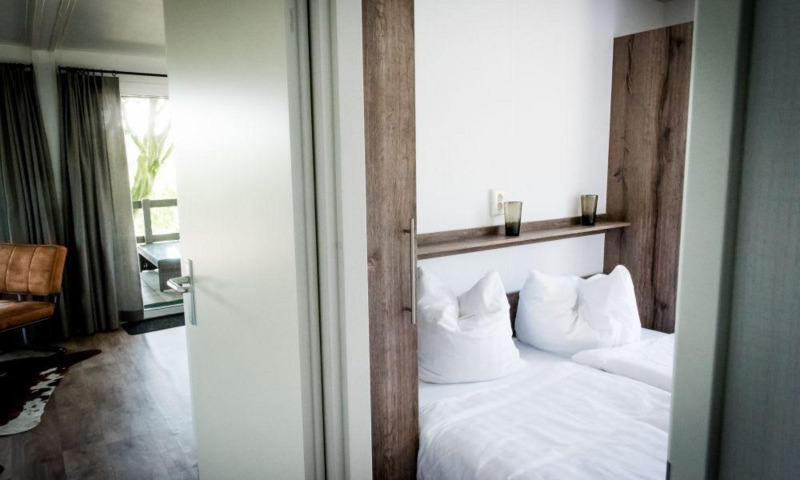 A modern lodge room with a double bed, white bedding, large windows with curtains, and a leather chair.