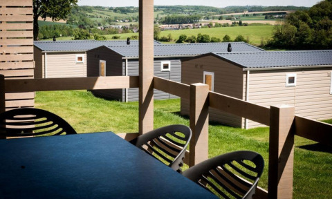 Blick von einer Veranda in einer Lodge auf moderne Ferienhäuser mit grüner Landschaft im Hintergrund.