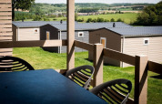 Vista dalla terrazza di un lodge, con case moderne e prati verdi nella campagna sullo sfondo.