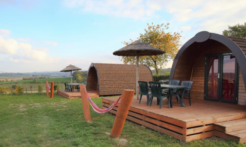 Cabañas Woodlodge con terrazas de madera, sillas exteriores y vistas panorámicas del campo al fondo.