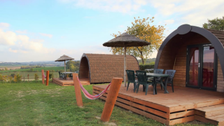 Cabañas Woodlodge con terrazas de madera, sillas exteriores y vistas panorámicas del campo al fondo.