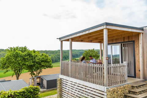Familia sentada en la terraza de un lodge Bellevue con vistas panorámicas al campo y zona verde.