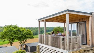 Famiglia seduta sulla veranda del Bellevue lodge con vista sui campi verdi e paesaggio collinare.