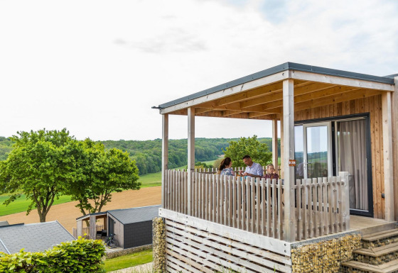 Famille attablée sur la terrasse en bois du lodge Bellevue, profitant d'une vue sur la campagne verdoyante.