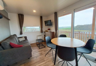 Moderne Bellevue lodge bij Gulperberg, Nederland, met sofa, eettafel en uitzicht op het landschap.