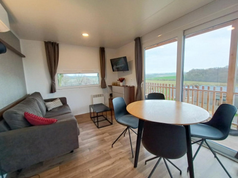 Moderne Bellevue lodge bij Gulperberg, Nederland, met sofa, eettafel en uitzicht op het landschap.