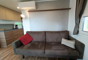 Moderne leefruimte in Bellevue-lodge bij Gulperberg, Nederland, met bruine zetel, kussens en keuken.