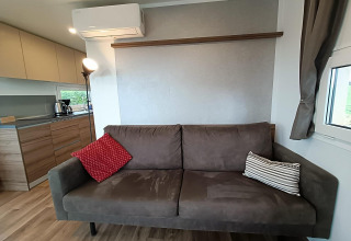 Moderne leefruimte in Bellevue-lodge bij Gulperberg, Nederland, met bruine zetel, kussens en keuken.