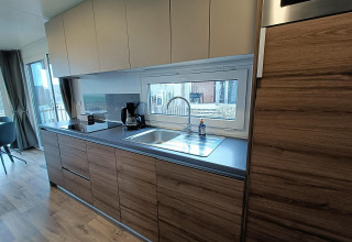 Moderne keuken in lodge Bellevue in Gulperberg, Nederland, met houten kasten en groot raam boven spoelbak.