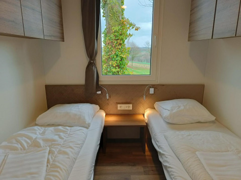Twee eenpersoonsbedden met witte lakens in een Bellevue-lodge bij Gulperberg, Nederland, met raamuitzicht.