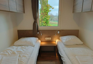 Twee eenpersoonsbedden met witte lakens in een Bellevue-lodge bij Gulperberg, Nederland, met raamuitzicht.