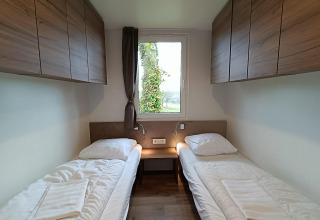 Twee eenpersoonsbedden met houten kasten en raam in een kamer bij Bellevue lodge op Gulperberg, Nederland.