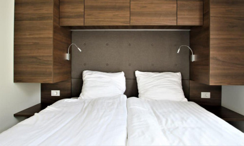 Cama moderna con sábanas blancas y paneles de madera en Bellevue, Gulperberg, Países Bajos.