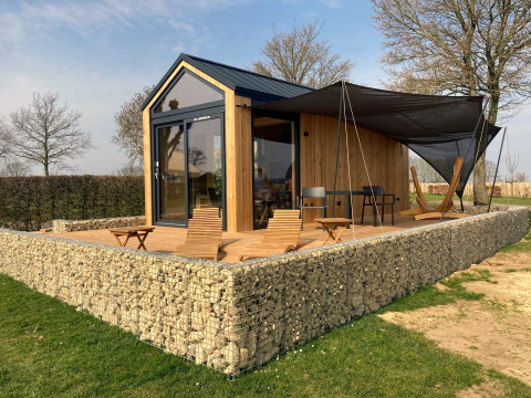 Ein modernes Tiny House Lodge mit Holzfassade, Steinmauer und Terrasse mit Stühlen und Hängematte.