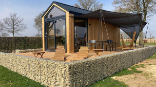 A modern Tiny House lodge with wooden siding, stone wall, outdoor deck, lounge chairs, and hammock.