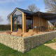 Et moderne Tiny House lodge med træbeklædning, stenmur og udendørs terrasse med stole og hængekøje.