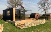 Moderne tiny house lodge met houten terras in Gulperberg, Nederland, tussen bomen en andere huisjes.