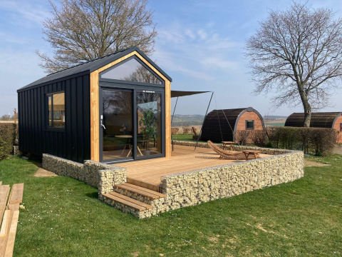 Moderne tiny house lodge met houten terras in Gulperberg, Nederland, tussen bomen en andere huisjes.