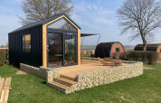 Moderne tiny house lodge met houten terras in Gulperberg, Nederland, tussen bomen en andere huisjes.